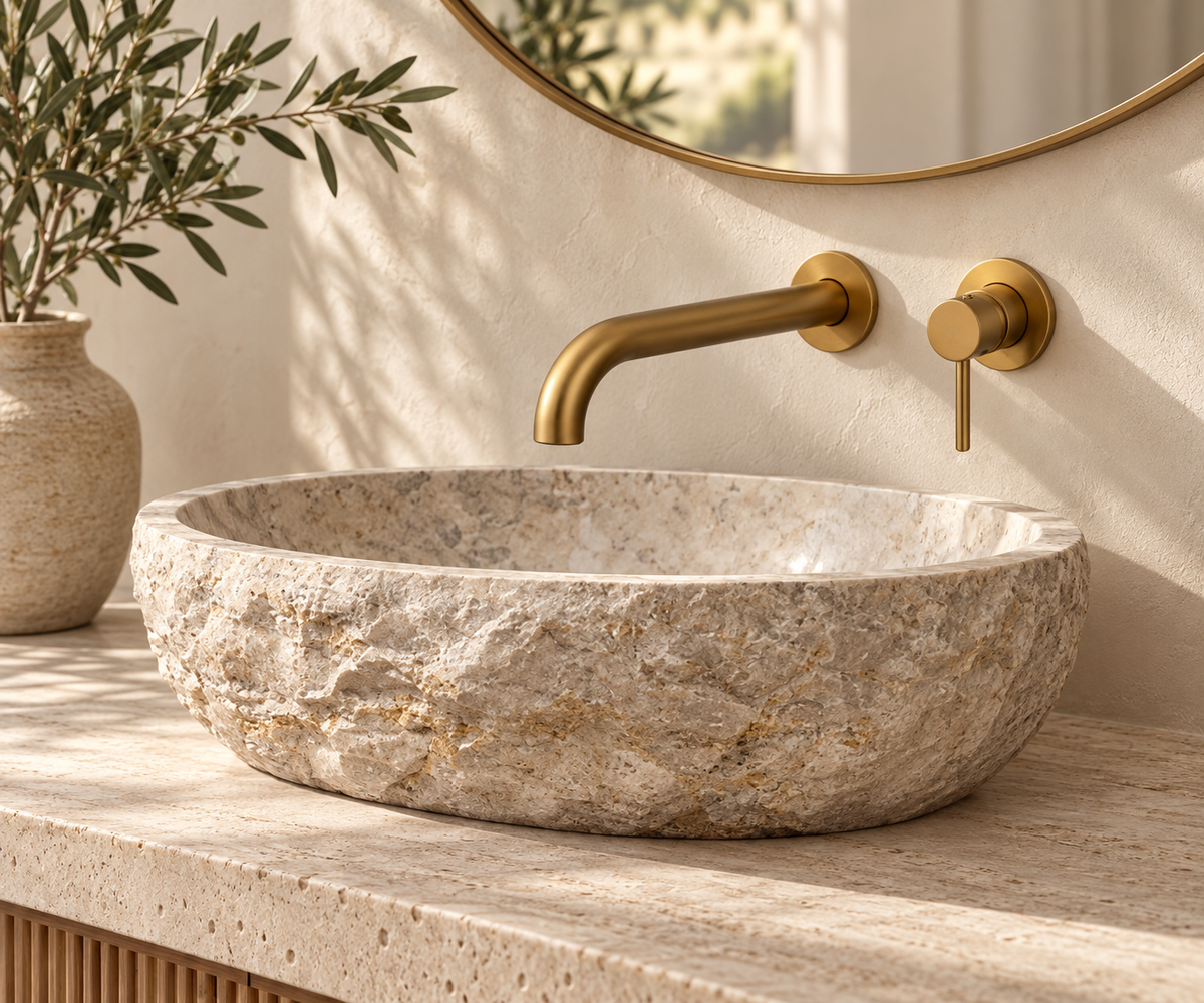 Lavabo GALBA de mármol beige natural con grifo mural dorado en un ambiente de baño